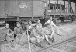 Corporal J Masterton and Leading Aircraftman L Moulden pause with a group of Chinese women carriage cleaners to watch a newly repaired engine of the Kowloon Railway on a test run in Hong Kong. This railway was immobilised during the Japanese occupation, services were restored under Royal Air Force supervision after the liberation. photo by RAF official photographer